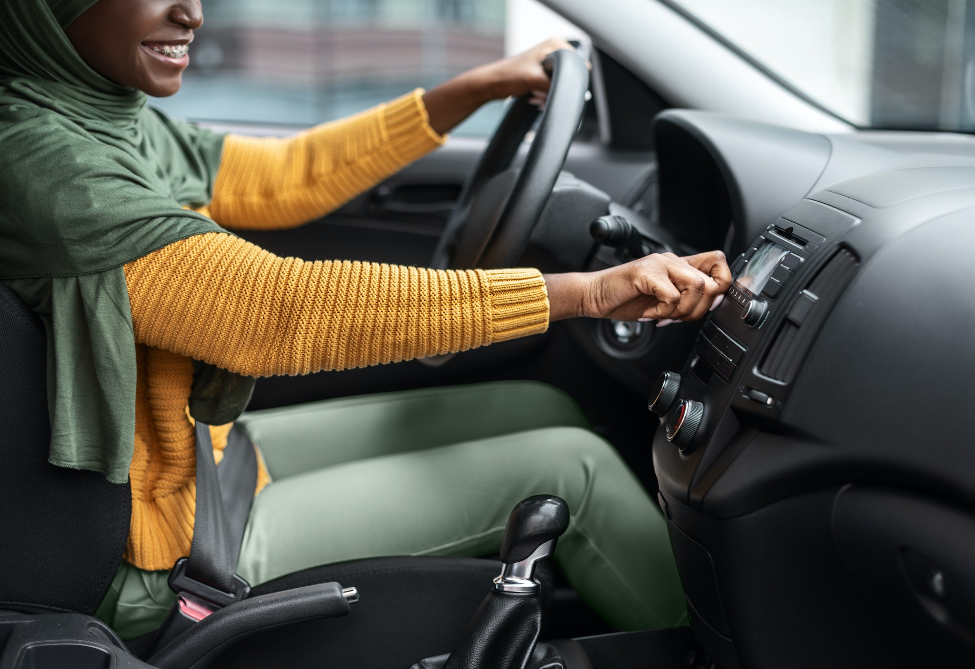 Unrecognizable black muslim woman turning on volume in car audio system